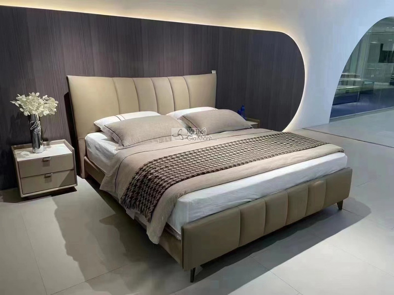 Giường ngủ bọc da hiện đại GIBJ108-18 chụp góc chếch, nổi bật đầu giường cao bọc da nâu be với đường may dọc. Khung giường…