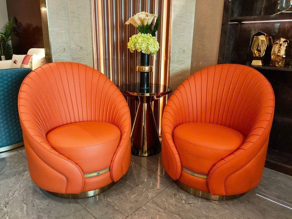 Hai ghế thư giãn GCQ628 màu cam đất đặt cạnh nhau trong không gian phòng khách luxury. Ghế bọc da nappa với họa tiết xếp n…
