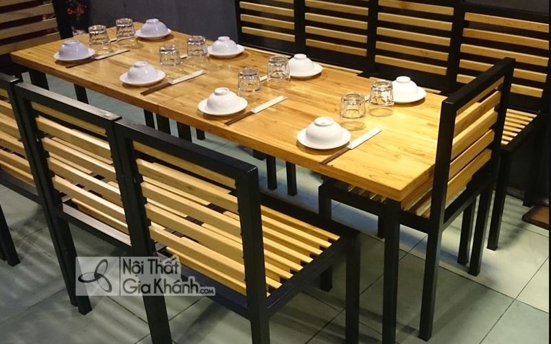 Bộ bàn ghế khung sắt đen, mặt bàn và lưng ghế ghép nan gỗ, bày sẵn bát đũa và ly