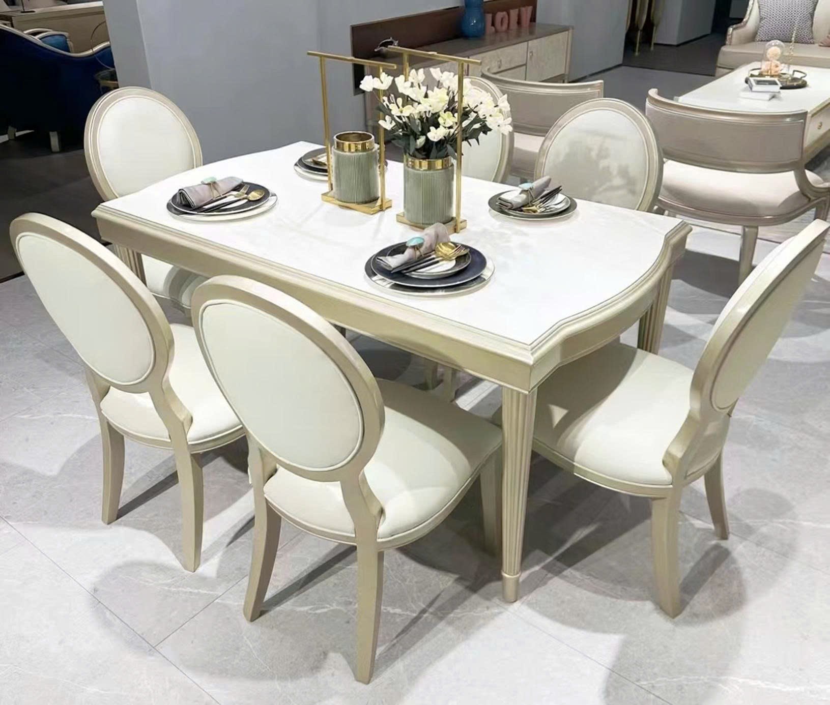 Bộ bàn ăn 6 ghế phong cách tân cổ điển, chụp từ góc cao trong không gian showroom. Bàn ăn hình chữ nhật bo tròn góc, mặt đ…