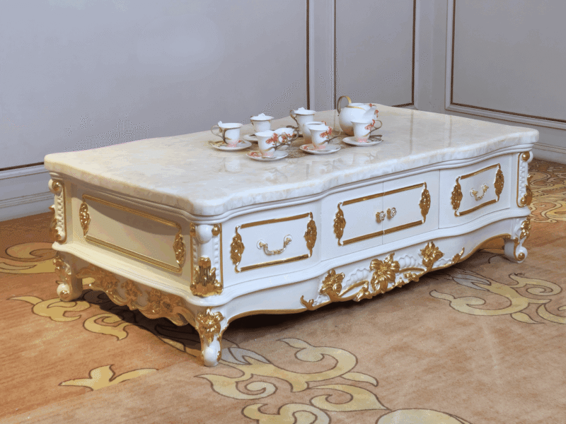 Bàn trà tân cổ điển BTA98-16 chụp từ góc thấp, hơi chếch bên phải, đặt trên thảm họa tiết vàng. Bàn có mặt đá tự nhiên vân…