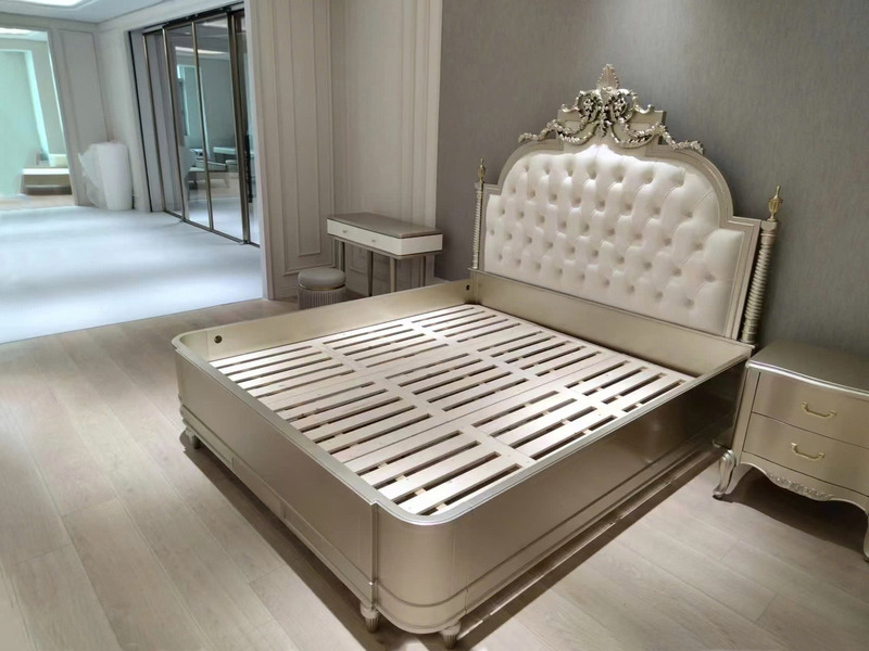 Giường ngủ 1m8 phong cách tân cổ điển, chụp từ góc chếch. Đầu giường bọc da nhân tạo màu kem, chần nút, kết hợp chạm khắc…