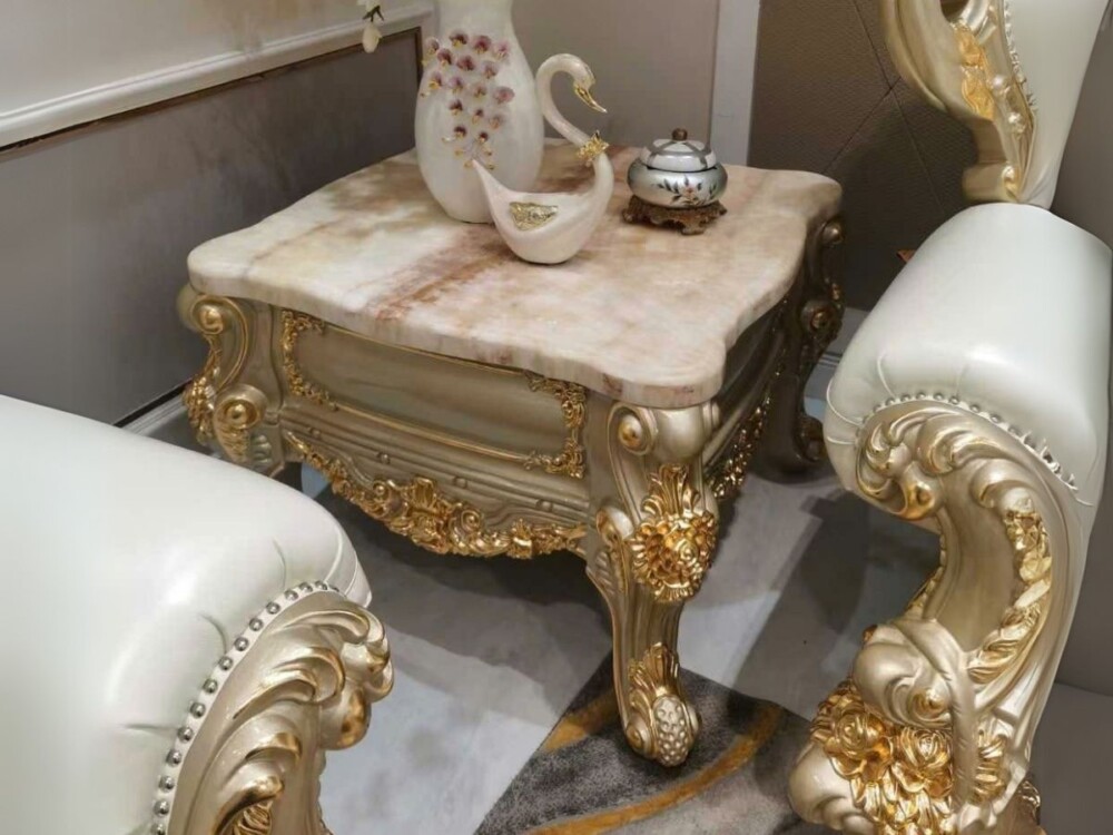 Hình ảnh bàn trà góc mặt đá tự nhiên BG801 được chụp từ trên xuống, đặt giữa hai chiếc ghế sofa đơn bọc da màu kem. Bàn nổ…