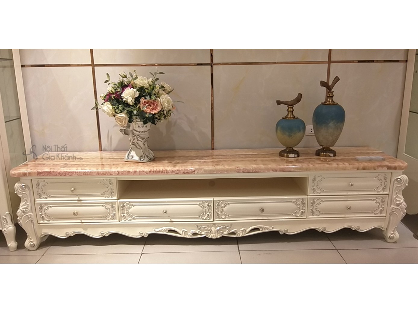 Hình ảnh cận cảnh kệ tivi KTA19-22 phong cách French White, làm nổi bật các đường nét chạm khắc uốn lượn mềm mại trên khun…
