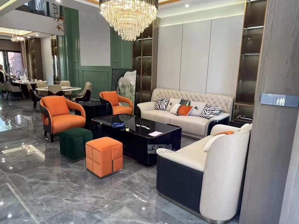 Góc nhìn rộng hơn của không gian phòng khách sang trọng, trưng bày bộ sofa SFQ626-1123. Hai ghế đơn màu cam và sofa băng m…
