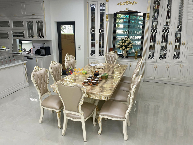 Toàn cảnh bộ bàn ăn BAT-29H với 8 ghế, chụp từ góc rộng hơn, cho thấy không gian phòng ăn liền kề khu vực bếp. Bàn ăn mặt…