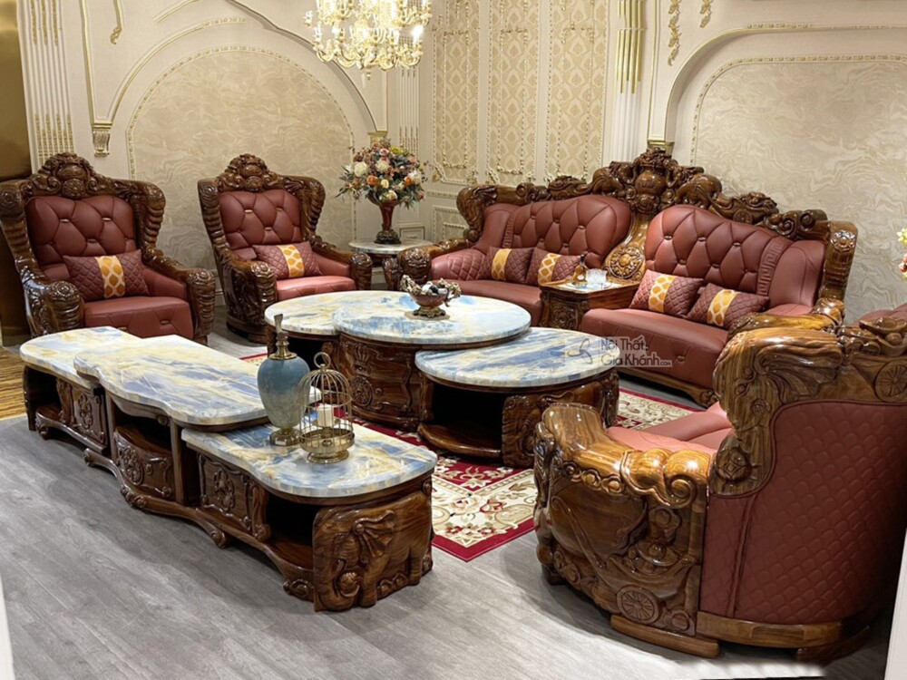 Góc chụp từ phía sau bên phải, tập trung vào sự sắp đặt của bộ sofa gỗ mun và bàn trà. Các chi tiết chạm khắc trên khung g…