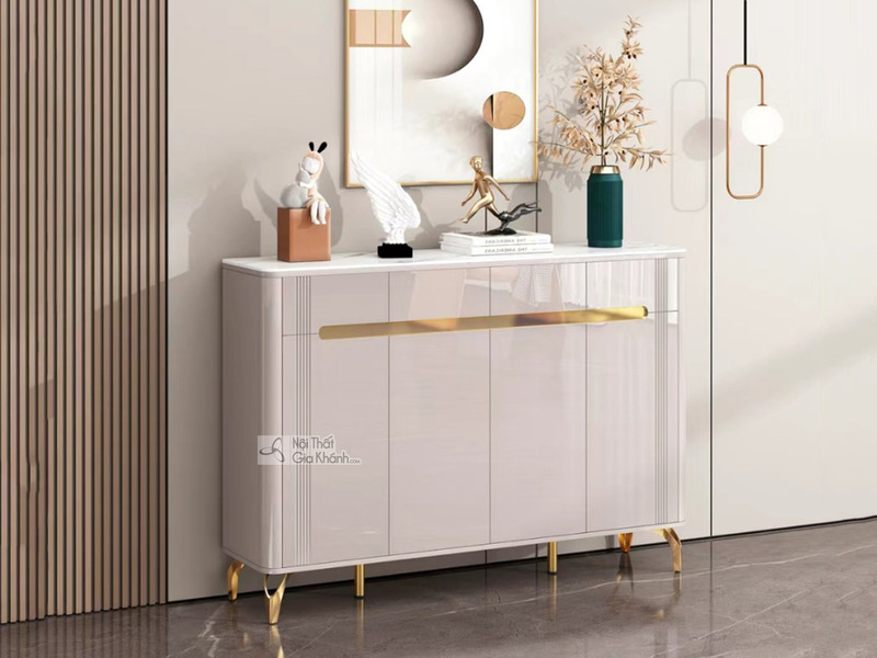 Tủ giày hiện đại TDEH167 được chụp chính diện, đặt trong không gian tiền sảnh hoặc hành lang. Tủ có màu trắng kem bóng, mặ…