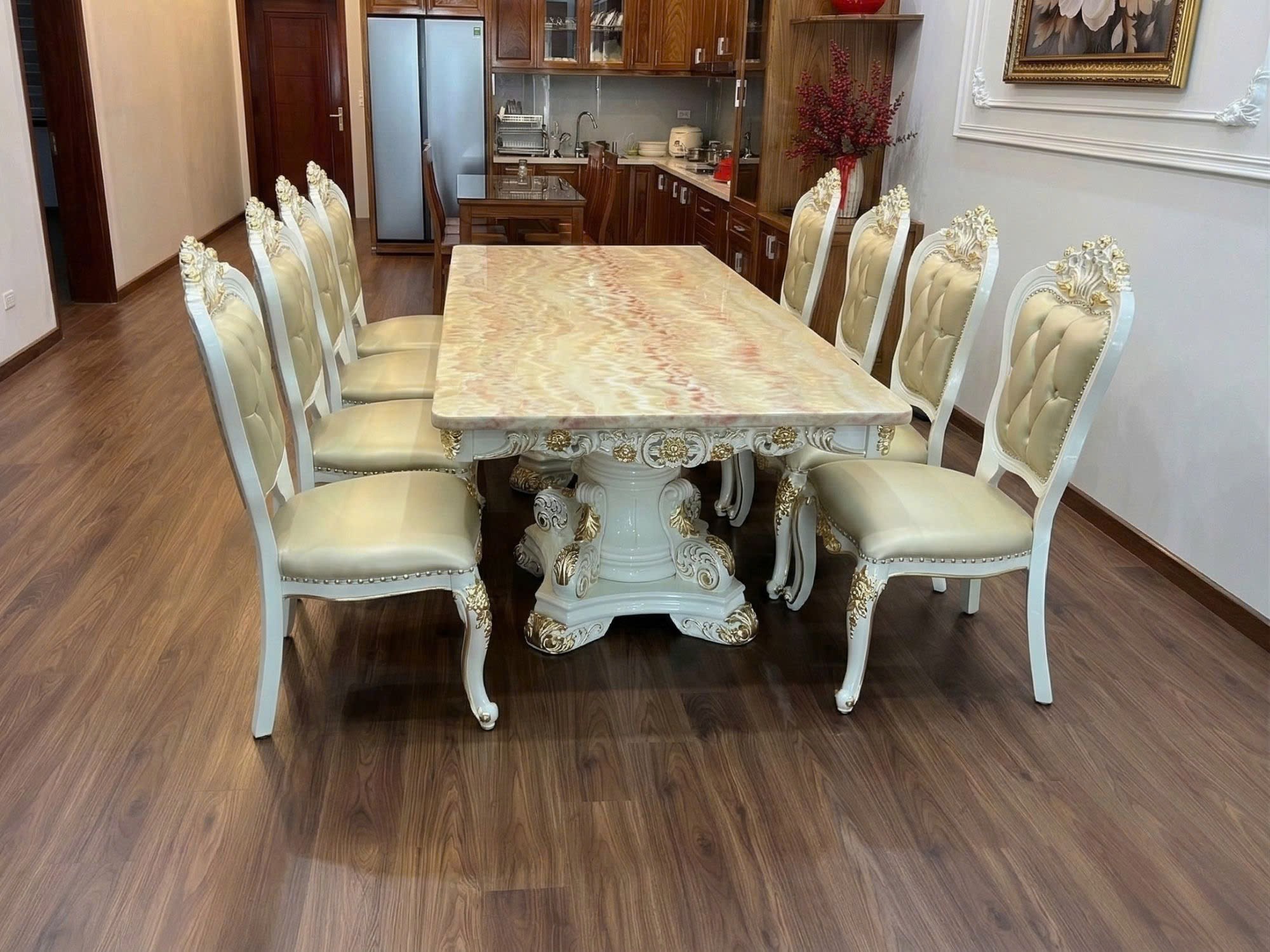 Bộ bàn ăn 10 ghế BAT66-24 chụp từ góc thấp, nhìn về phía khu vực bếp hiện đại. Bàn ăn mặt đá Hồng ngọc long nhân tạo, chân…