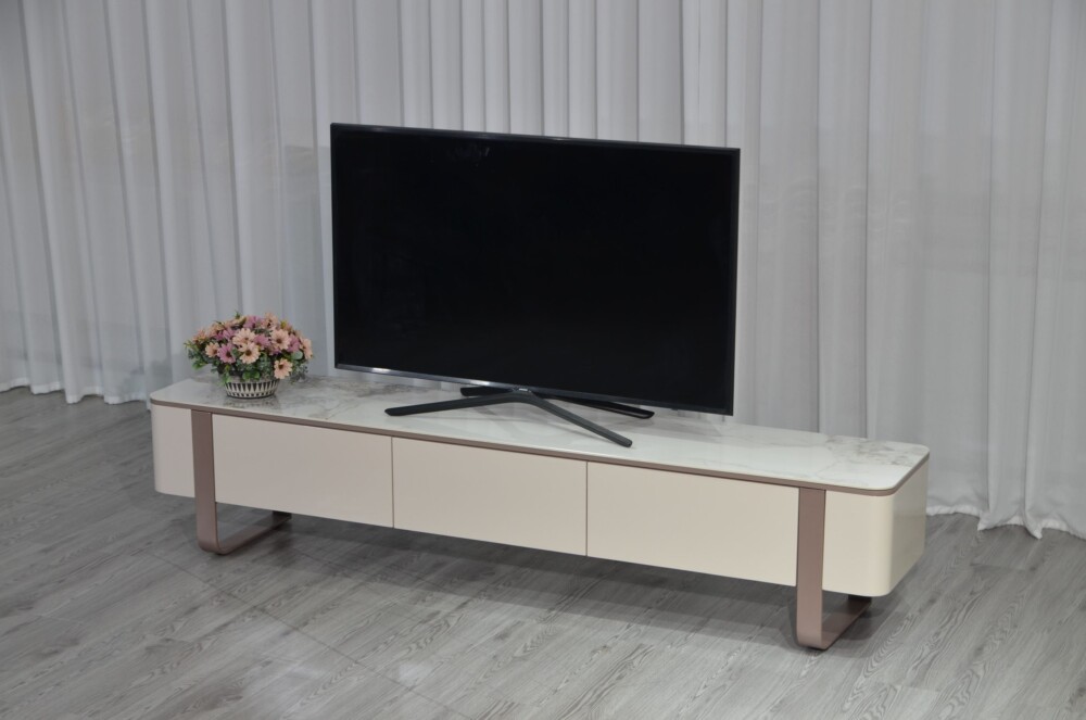 Kệ tivi KTKD8221-20 nhìn từ góc nghiêng, đặt trong phòng khách với rèm cửa trắng. Kệ có mặt đá phiến Chanel, thân tủ màu k…