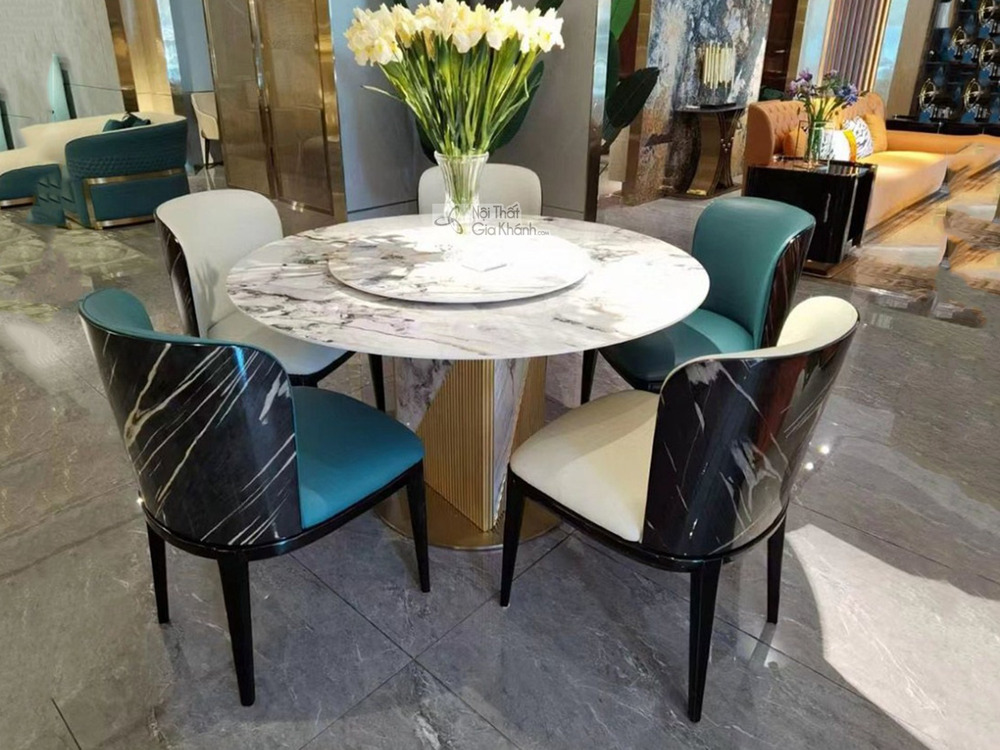 Bàn ăn tròn mặt đá phiến trắng vân xám với mâm xoay trung tâm, đặt trong không gian showroom sang trọng. Chân bàn hình trụ…