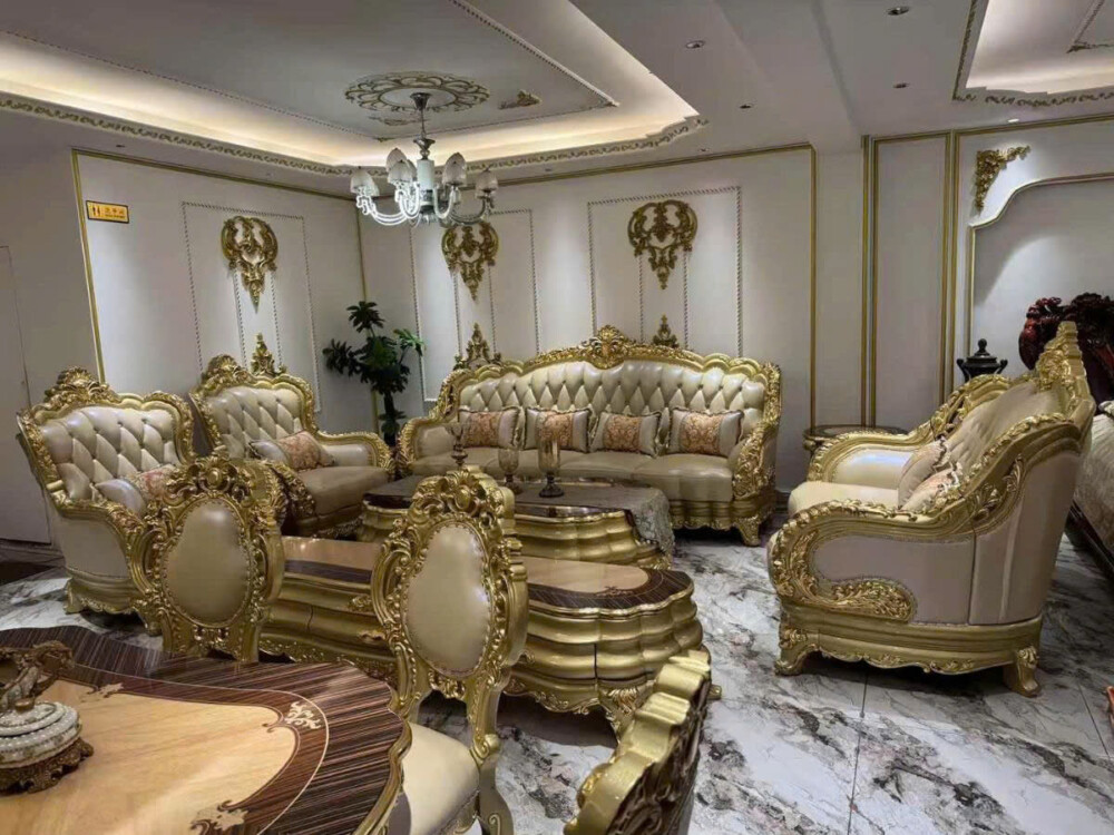 Toàn cảnh bộ sofa tân cổ điển SB990-1124 màu kem bọc da, với khung gỗ Sồi tự nhiên chạm khắc họa tiết dát vàng nổi bật, đặ…