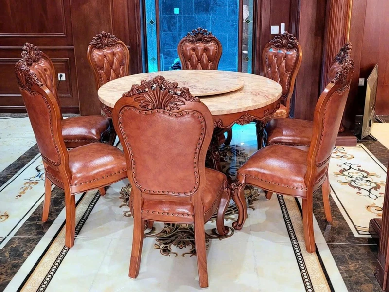 Bộ bàn ăn tròn tân cổ điển với 6 ghế được sắp xếp quanh bàn, chụp từ góc hơi chếch phía trước. Bàn có mặt đá màu vàng kem…