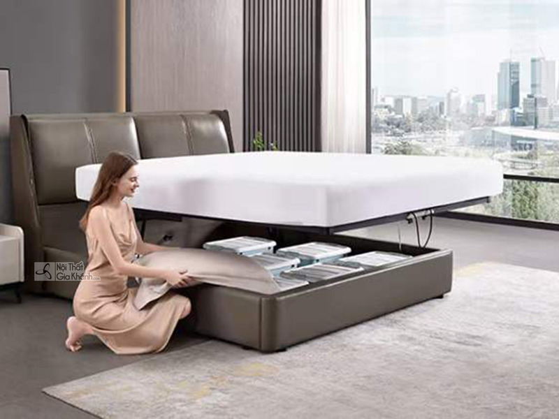 Giường ngủ thông minh GI02GK-18 màu nâu xám, chụp cận cảnh tính năng hộc đựng đồ dưới đệm. Một phụ nữ đang sắp xếp chăn ga…