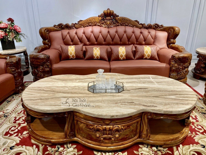 Cận cảnh bàn trà chính hình bầu dục với mặt đá cẩm thạch vân mây tự nhiên, đặt trước ghế sofa băng dài. Khung bàn làm từ g…