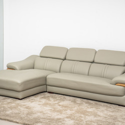 Sofa da góc phải màu be/ghi sáng, chụp từ góc thấp phía trước bên trái, đặt trên thảm lông màu kem trong không gian phòng…