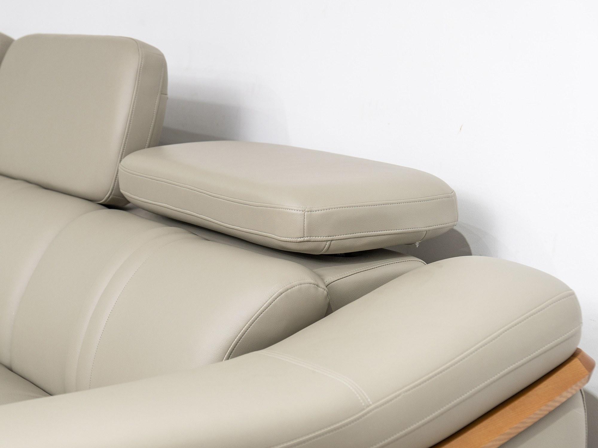 Cận cảnh phần góc nối và tựa đầu của sofa da màu be/ghi sáng, chụp từ góc trên xuống. Nổi bật sự mềm mại của đệm, đường né…