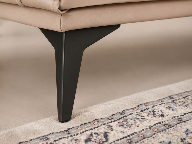 Cận cảnh chân sofa kim loại màu đen của bộ AURELIA, thiết kế hình thang ngược, đặt trên thảm trải sàn họa tiết. Chi tiết c…
