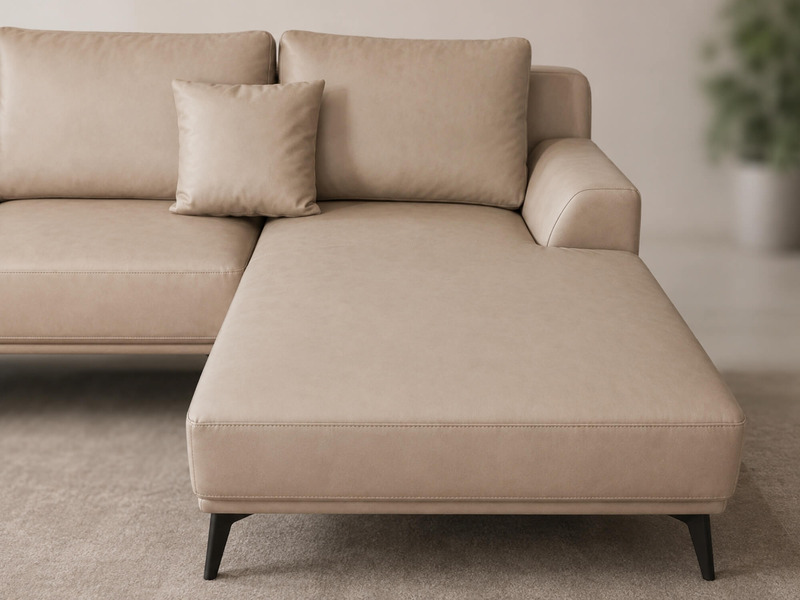 Cận cảnh phần góc chữ L của sofa da AURELIA màu be nhạt, chụp từ góc thấp. Thiết kế tối giản với các đường nét vuông vắn…