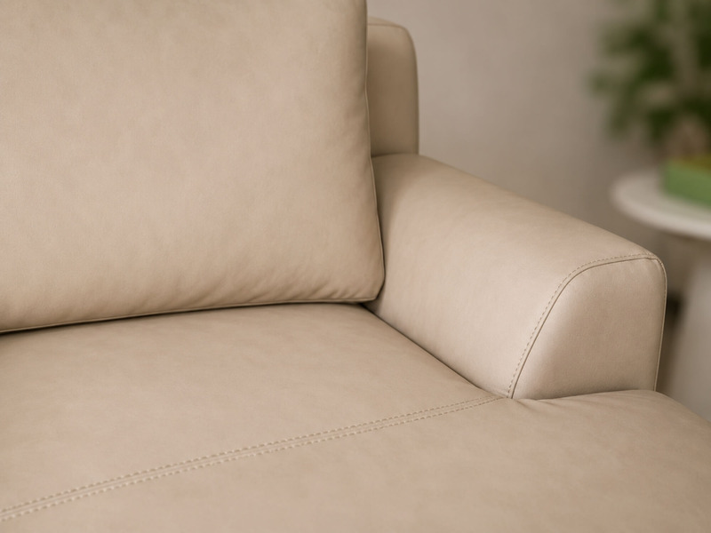 Cận cảnh tay vịn và đệm tựa lưng của sofa da AURELIA màu be nhạt, chụp nghiêng. Tay vịn có đường cong nhẹ nhàng, kết hợp v…