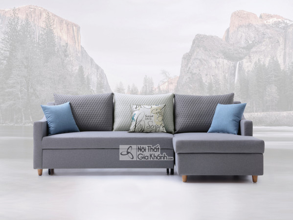 Một chiếc ghế giường sofa góc chữ L màu xám hiện đại, được chụp chính diện trên nền trắng với phông nền núi mờ ảo. Sofa có…