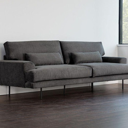 Sofa băng bọc vải màu xám đậm, chụp góc nghiêng từ phía trước, thể hiện kiểu dáng hiện đại với đường nét thanh thoát. Sofa…