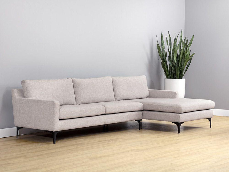 Sofa lệch góc bọc vải cao cấp màu be nhạt, kiểu dáng hiện đại với chân thép không gỉ sơn đen mờ. Sofa được đặt trong không…