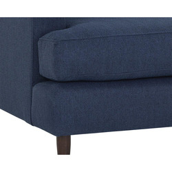 Cận cảnh phần chân ghế gỗ walnut màu nâu sẫm và góc đệm ngồi của sofa băng bọc vải màu xanh đậm. Hình ảnh làm nổi bật chất…