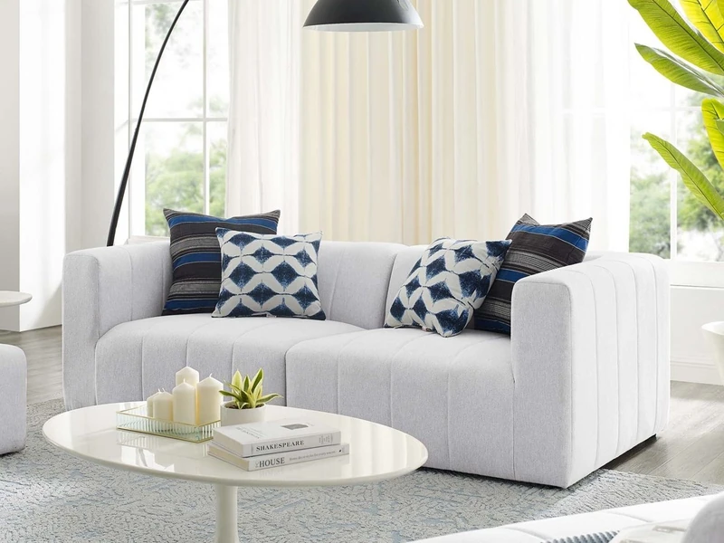 Sofa băng hai chỗ màu trắng xám, thiết kế không chân hiện đại, đặt trong phòng khách tràn ngập ánh sáng. Góc chụp chính di…