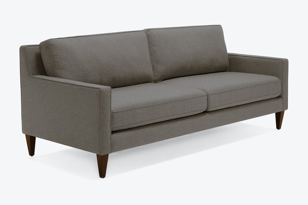 Sofa băng bọc vải màu xám tro, chụp nghiêng từ phía trước bên phải, trên nền trắng. Thiết kế tối giản, hiện đại với tay vị…