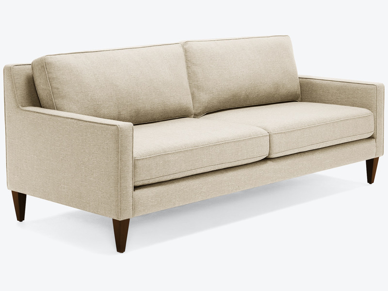 Sofa băng bọc vải màu be nhạt, chụp nghiêng từ phía trước bên phải, nổi bật trên nền trắng. Sofa có thiết kế hiện đại với…