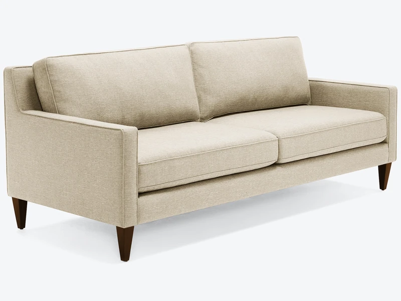 Sofa băng bọc vải màu be nhạt, chụp nghiêng từ phía trước bên phải, nổi bật trên nền trắng. Sofa có thiết kế hiện đại với…