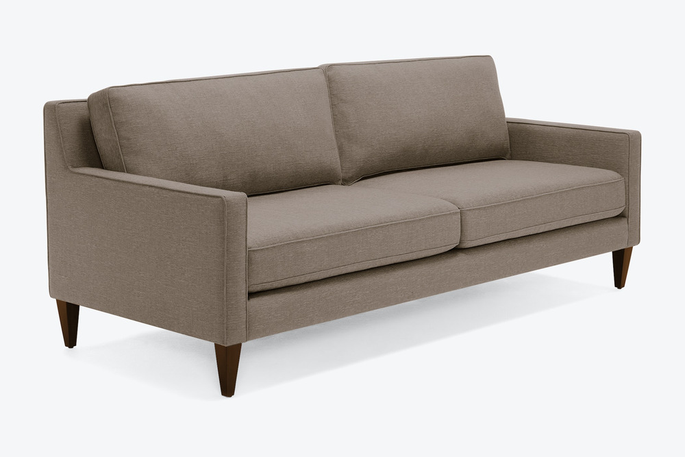 Sofa băng bọc vải màu nâu xám trung tính, chụp nghiêng từ phía trước bên phải. Thiết kế tinh giản, hiện đại với hai đệm ng…