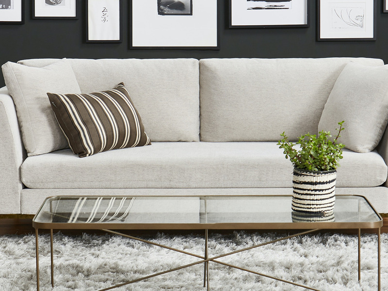 Sofa băng Ainsley SF-369 bọc vải màu be nhạt, đặt trong không gian phòng khách hiện đại với tường màu đen và các bức tranh…