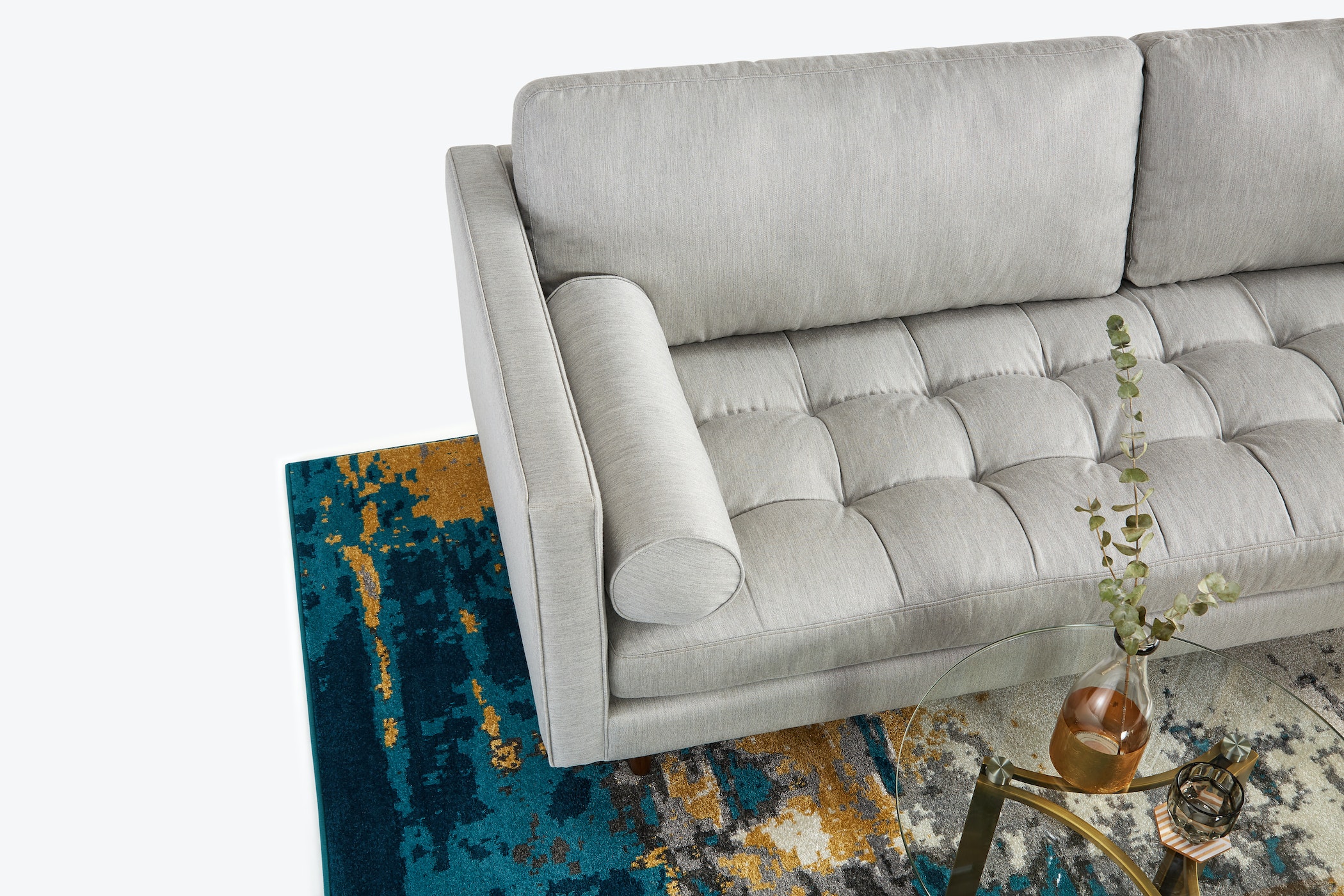 Góc nhìn từ trên xuống của sofa băng 3 chỗ bọc vải màu xám nhạt, đặt trên thảm họa tiết xanh và cam. Bố cục độc đáo, làm n…
