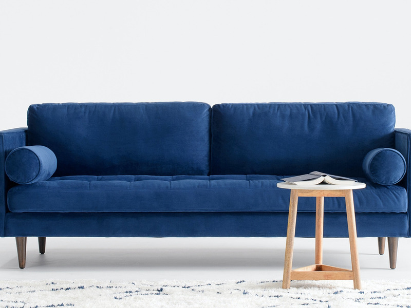 Sofa băng 3 chỗ bọc vải màu xanh navy nổi bật, đặt giữa phòng khách với thảm họa tiết và bàn trà gỗ nhỏ. Góc chụp chính di…