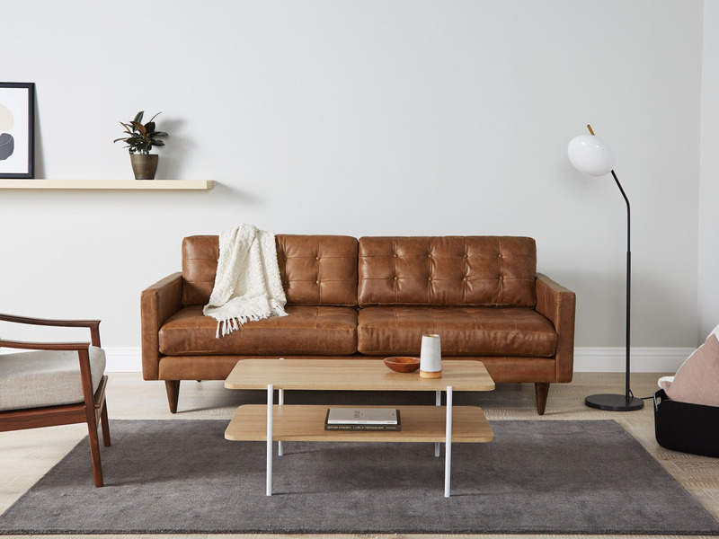 Sofa băng bọc da màu nâu caramel, phong cách mid-century, đặt trong phòng khách hiện đại. Sofa có thiết kế tối giản với ch…