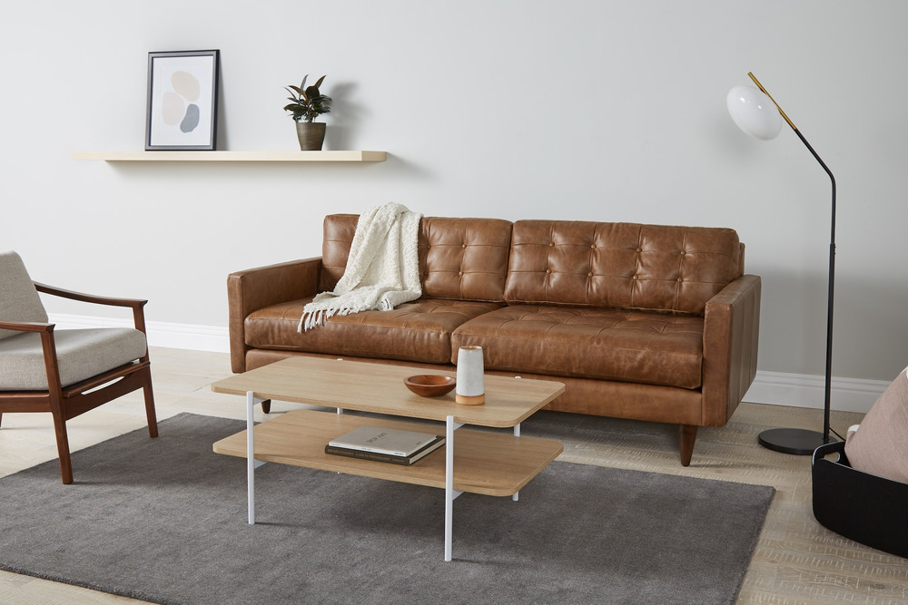 Sofa băng bọc da màu nâu caramel, đặt trong không gian phòng khách hiện đại với ánh sáng tự nhiên. Sofa có thiết kế tối gi…