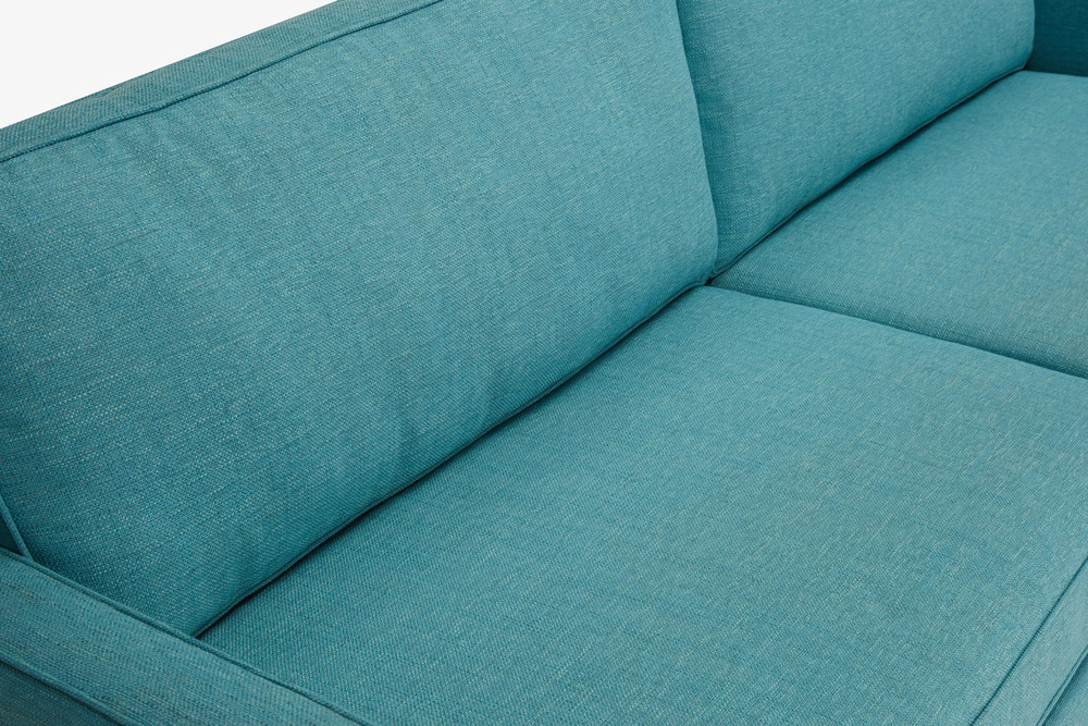 Cận cảnh góc đệm ngồi và tựa lưng của sofa băng bọc vải màu xanh ngọc tươi sáng. Chất liệu vải dệt thô với các đường may t…
