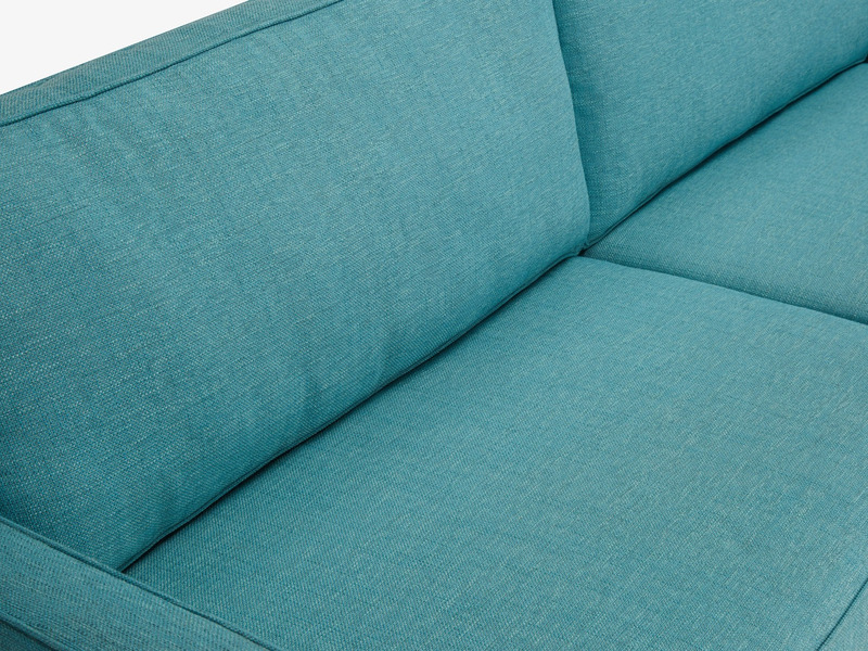 Cận cảnh góc đệm ngồi và tựa lưng của sofa băng bọc vải màu xanh ngọc tươi sáng. Chất liệu vải dệt thô với các đường may t…