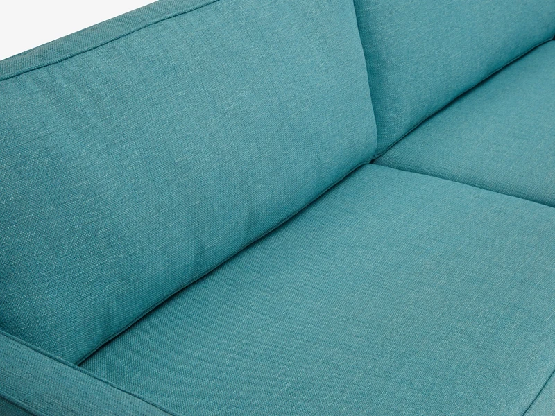Cận cảnh góc đệm ngồi và tựa lưng của sofa băng bọc vải màu xanh ngọc tươi sáng. Chất liệu vải dệt thô với các đường may t…