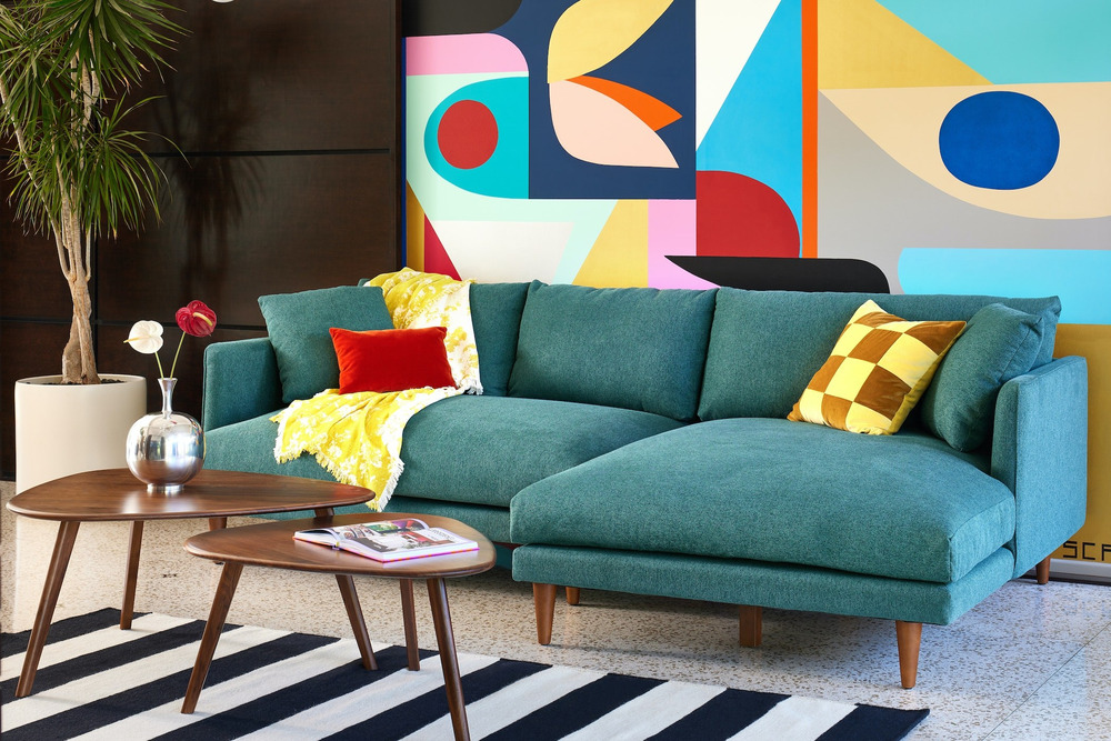 Sofa góc chữ L Lewis SF-489 bọc vải màu xanh ngọc đậm, nổi bật trong không gian phòng khách với bức tường trang trí nghệ t…