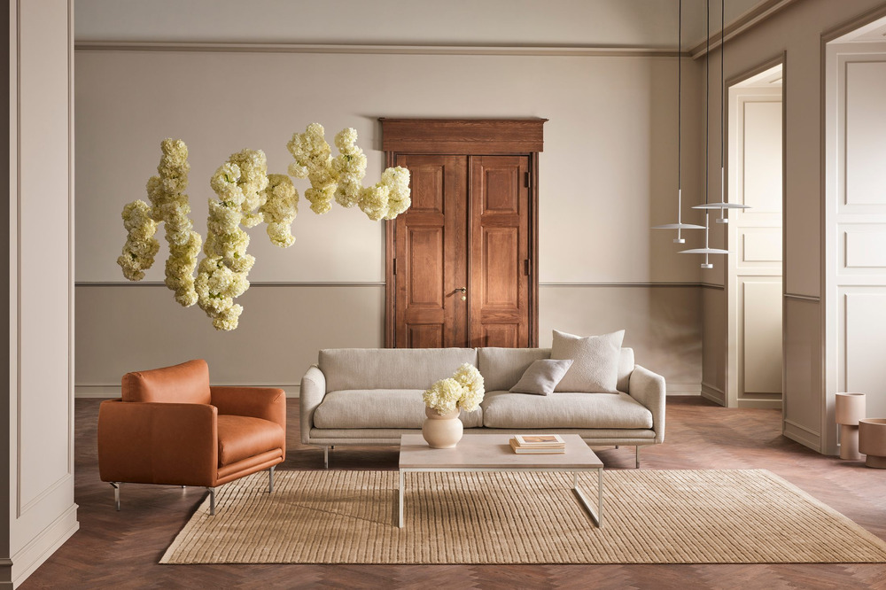 Sofa bọc vải màu be nhạt được bố trí trong phòng khách phong cách tân cổ điển, với tường màu kem và sàn gỗ xương cá. Không…
