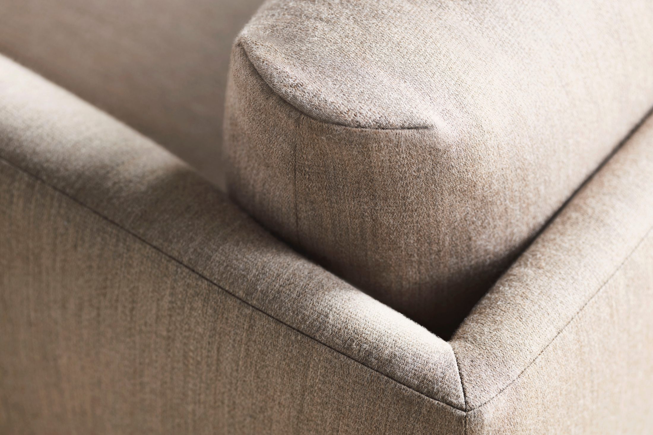 Góc cận cảnh chi tiết đường may và kết cấu của phần đệm ngồi và tay vịn sofa bọc vải màu be nhạt. Các đường nét mềm mại, b…