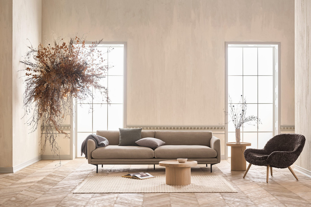 Sofa bọc vải màu xám đậm với thiết kế hiện đại, đặt trong phòng khách có sàn gỗ xương cá và tường màu kem. Không gian được…