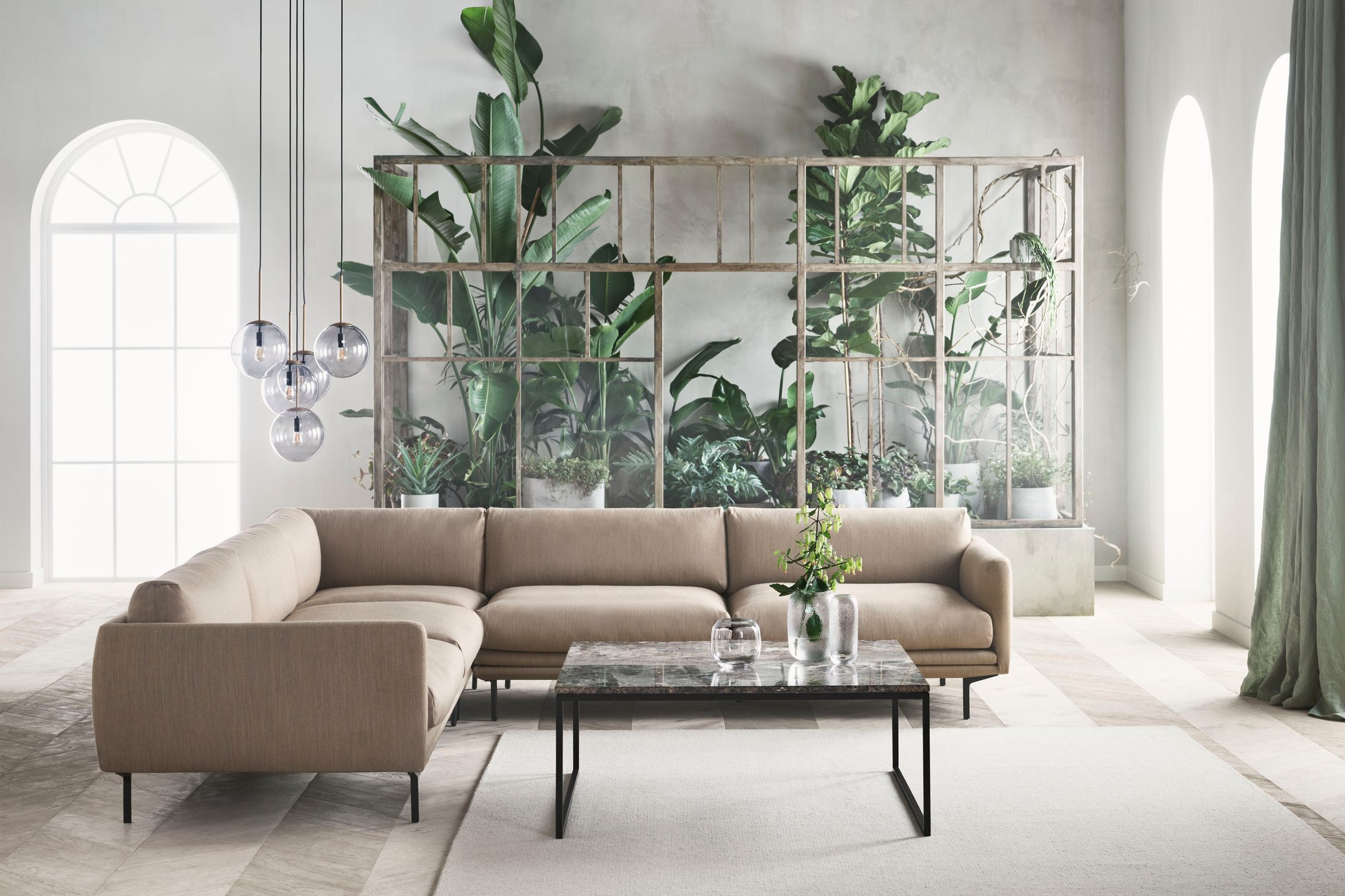 Sofa góc bọc vải màu be nhạt, thiết kế hiện đại, đặt trong phòng khách tràn ngập ánh sáng tự nhiên từ cửa sổ vòm lớn. Khôn…