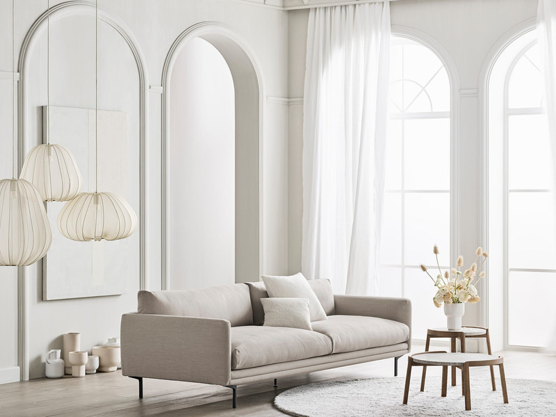 Sofa băng bọc vải màu be nhạt, kiểu dáng đương đại, đặt trong không gian phòng khách hiện đại với tường trắng, cửa vòm lớn…