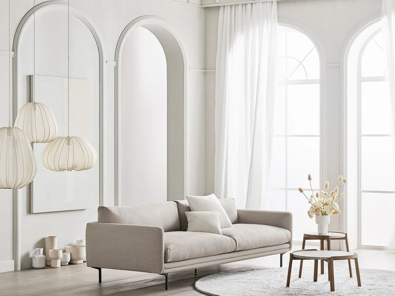 Sofa băng bọc vải màu be nhạt, kiểu dáng đương đại, đặt trong không gian phòng khách hiện đại với tường trắng, cửa vòm lớn…