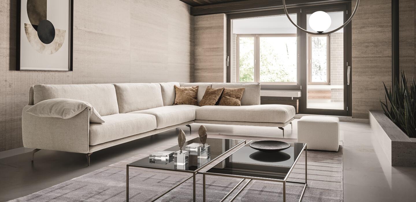 Sofa góc chữ L bọc vải màu kem nhạt, đặt trong không gian phòng khách hiện đại. Sofa có tay vịn hơi xòe, đệm ngồi êm ái và…