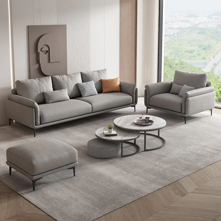 Bộ sofa Trudie SF-219 màu xám nhạt bao gồm sofa băng, ghế đơn và đôn, đặt trong không gian phòng khách rộng rãi. Bố cục tổ…